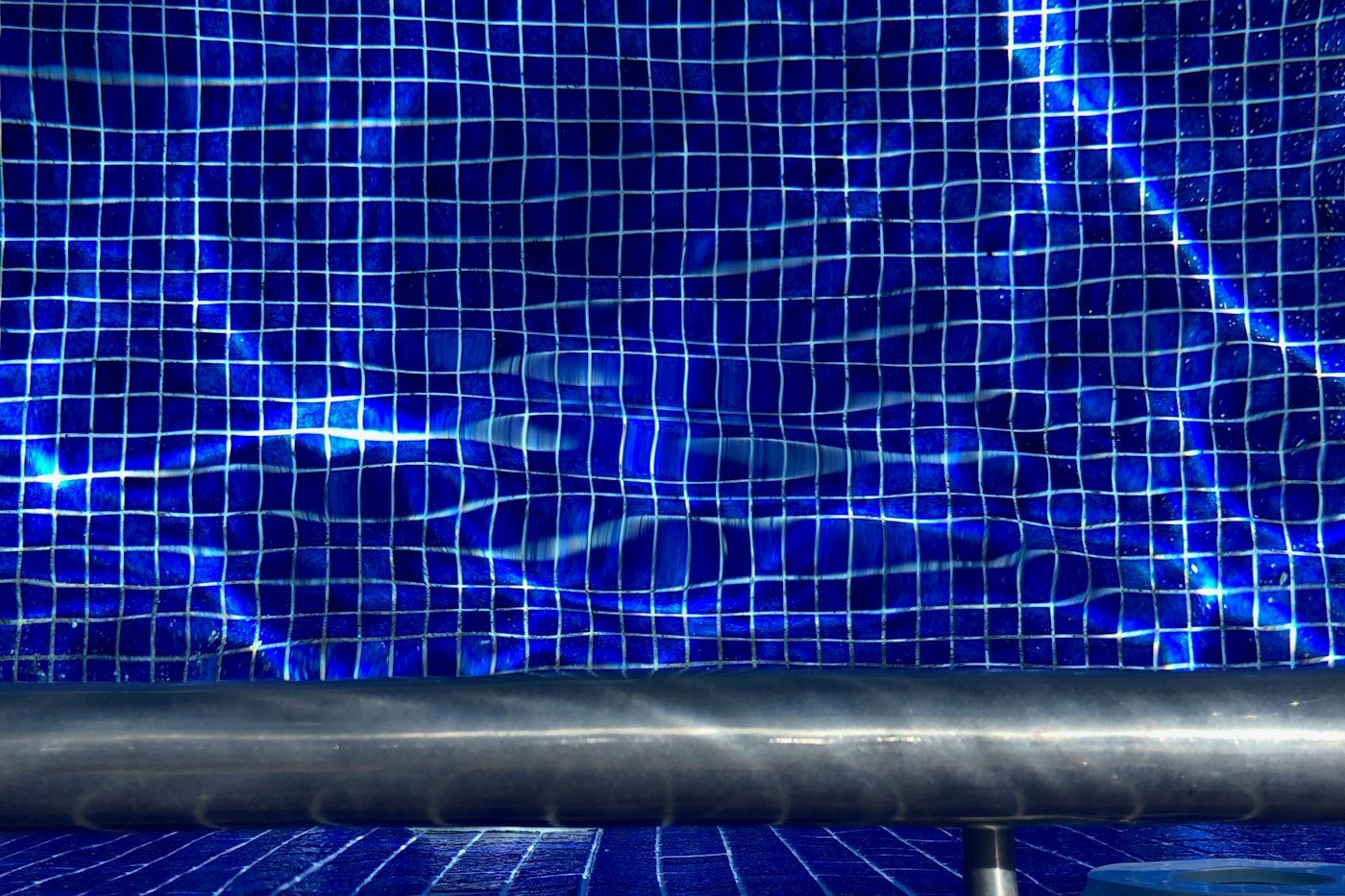 阳光照在蓝色马赛克瓷砖的泳池水面上